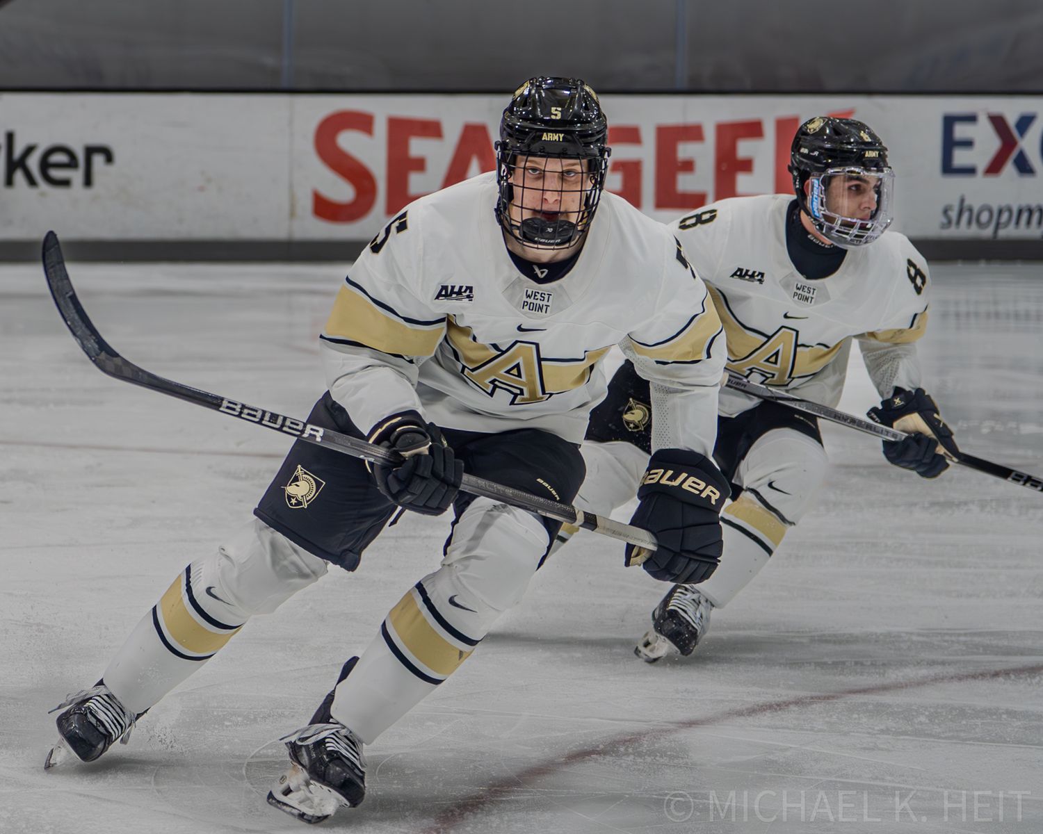 Army West Point Hockey players in white uniforms lean forward while skating during competitive game.