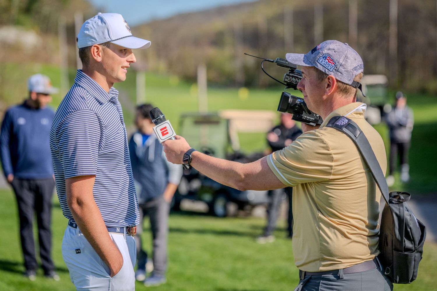 Golfer being interviewed on course by TV cameraman with ESPN microphone at outdoor golf event.