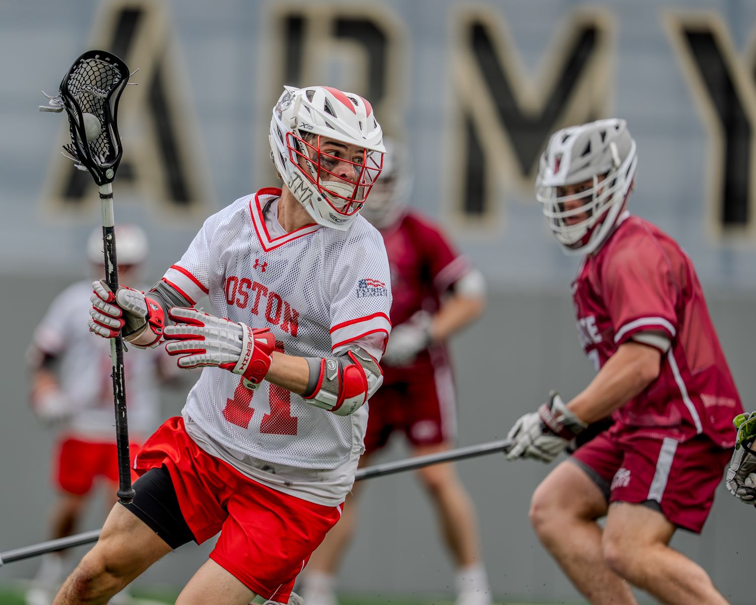 College lacrosse players from opposing teams compete for ball control during a match.