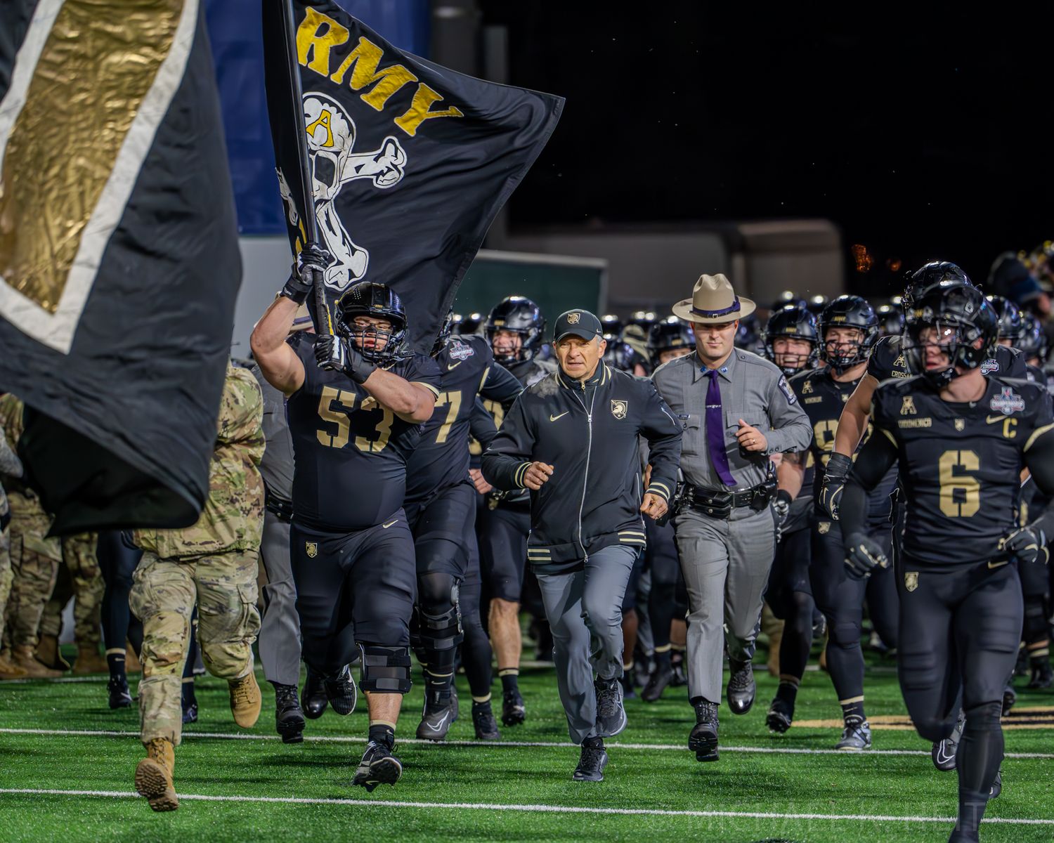 Navy uniformed players run onto football field during team entrance.