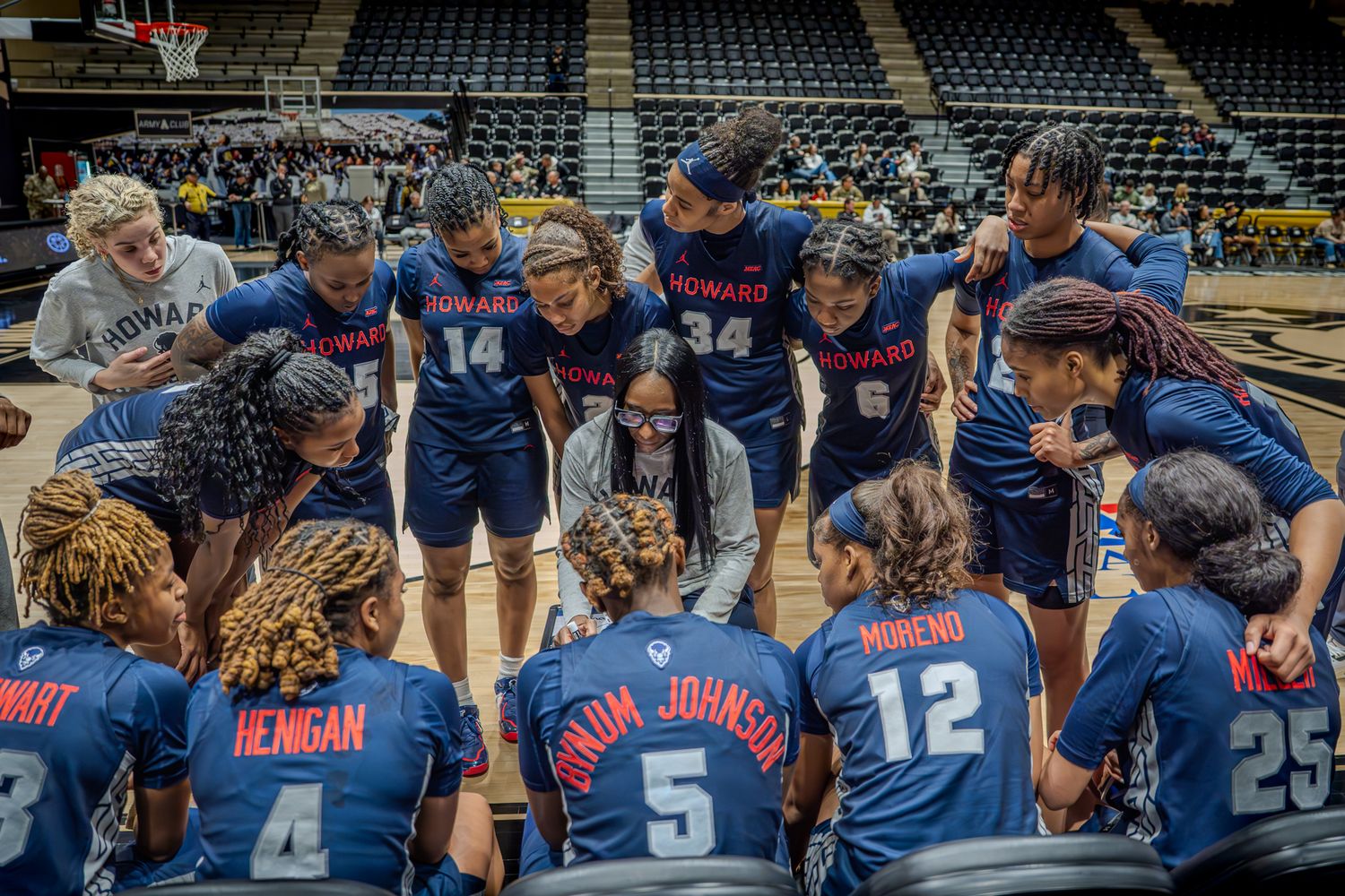 A basketball team huddles together on the court wearing navy blue uniforms during a game.