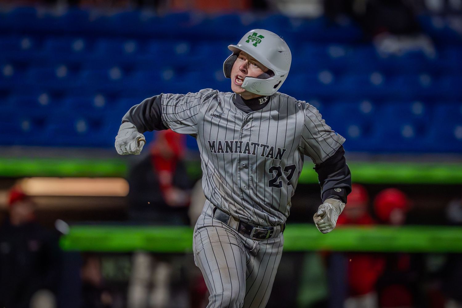Baseball player in pinstriped uniform swings bat during nighttime game with stadium lights visible in background.