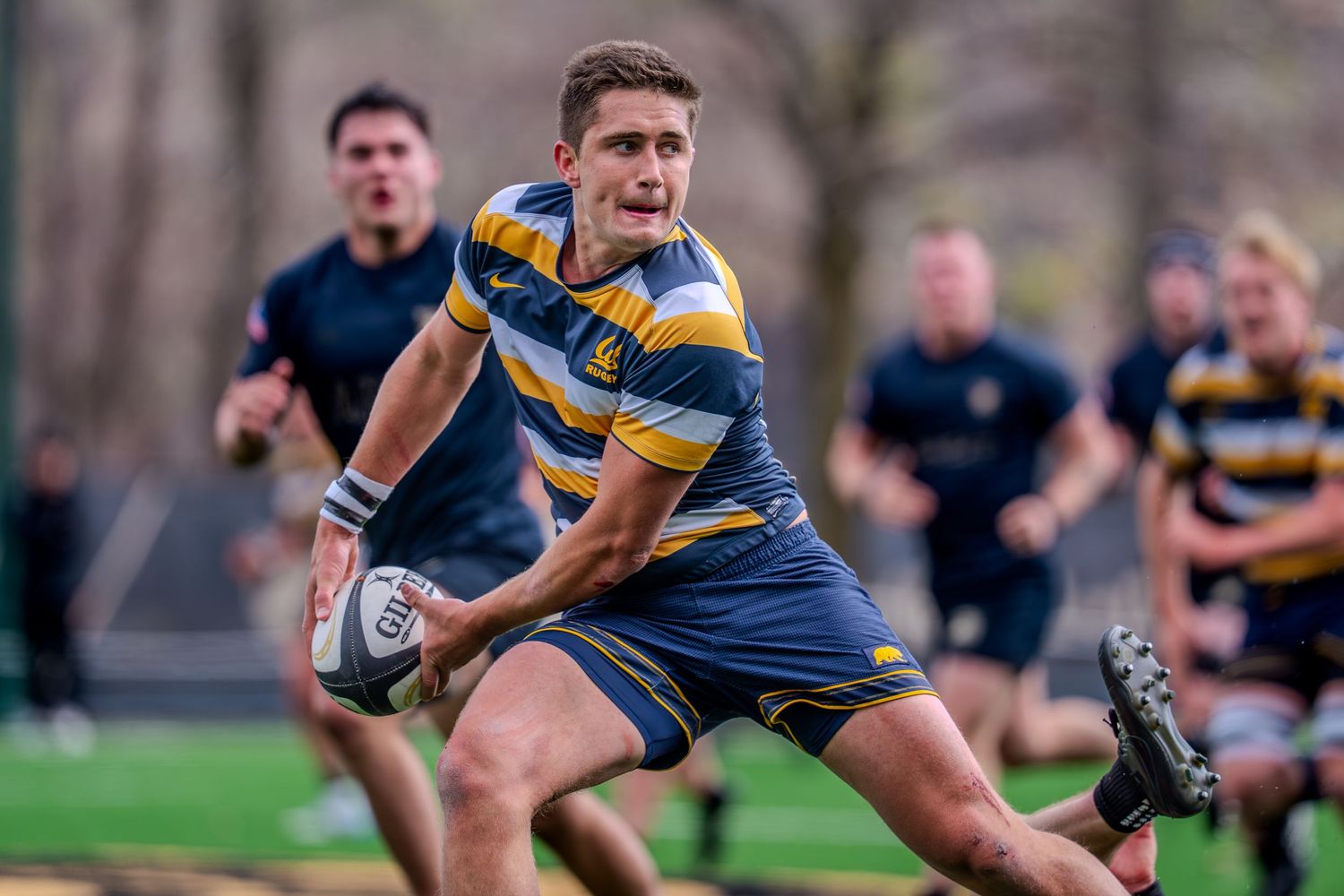 Rugby player in blue and yellow striped jersey makes a diving pass during an intense match.