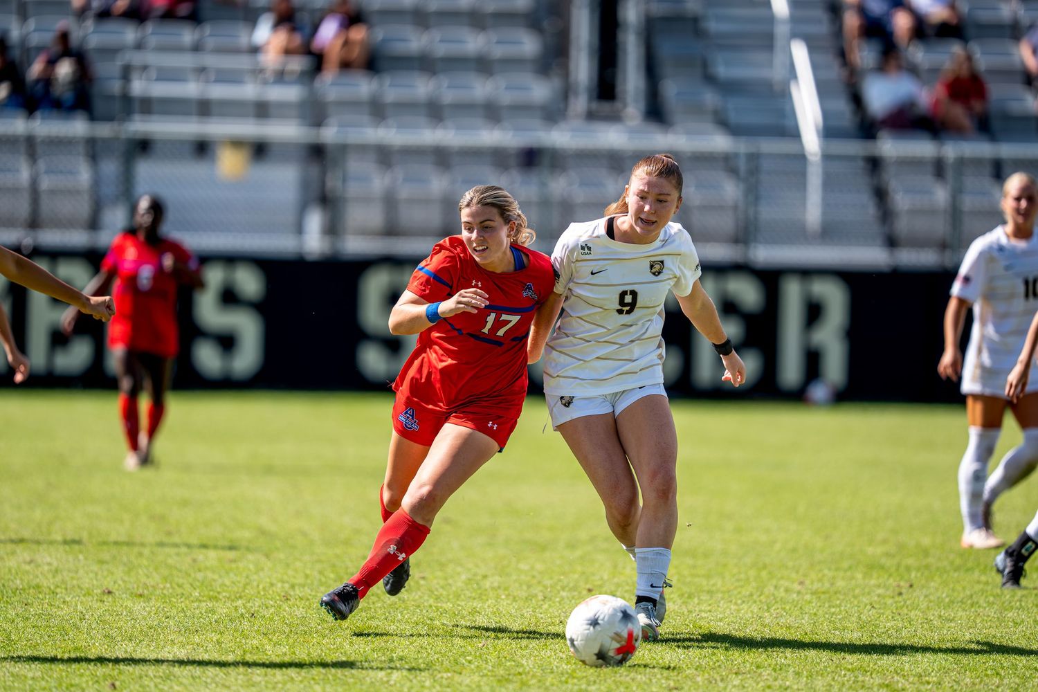 Two female soccer players compete for the ball during a match, one in red jersey #17 and another in white #9.