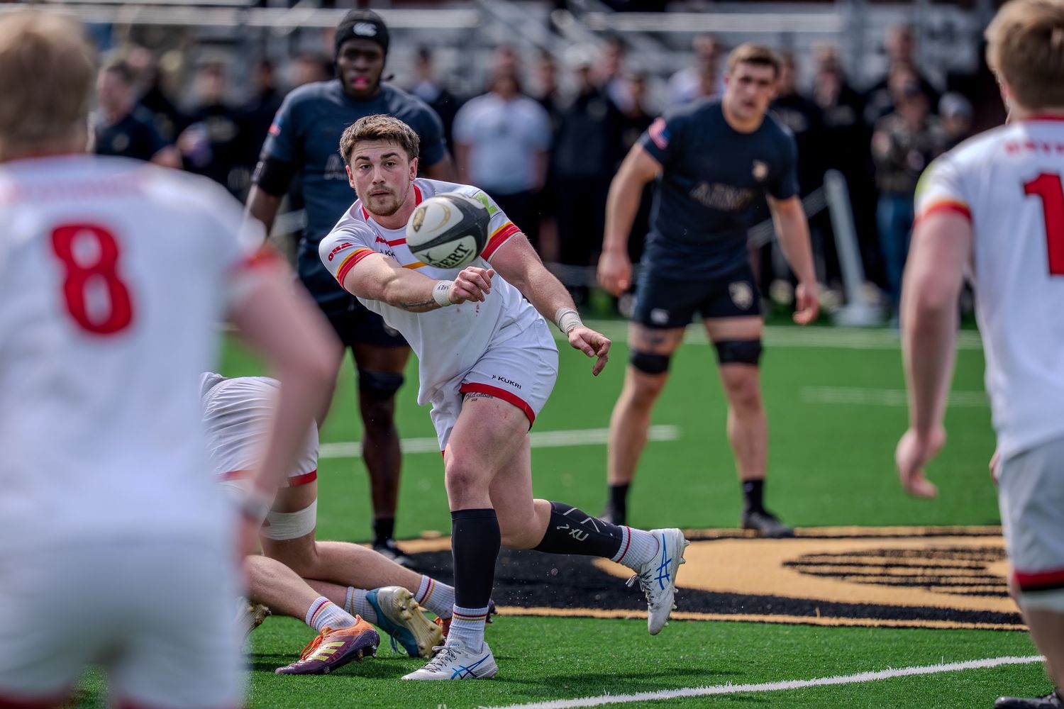 Rugby players compete for possession during an intense match on the field as teammates look on from both sides.