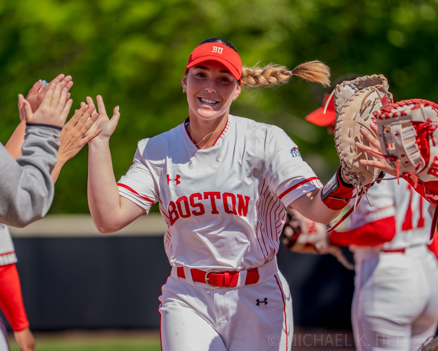 Softball player in Boston uniform celebrates with teammates on the field during a game.