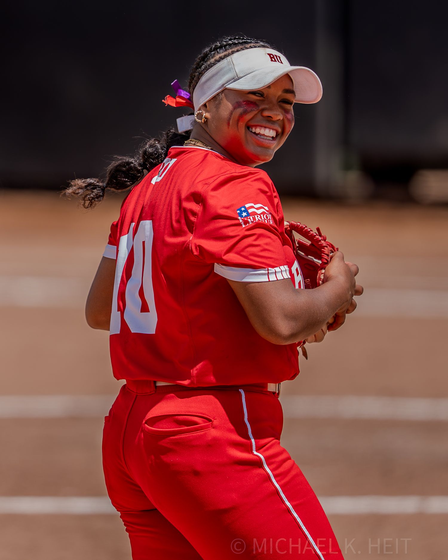 Softball player in red jersey smiles joyfully during game.