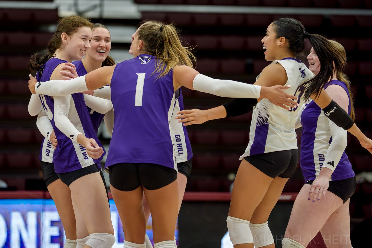 Volleyball players in purple uniforms celebrating a point during a match.