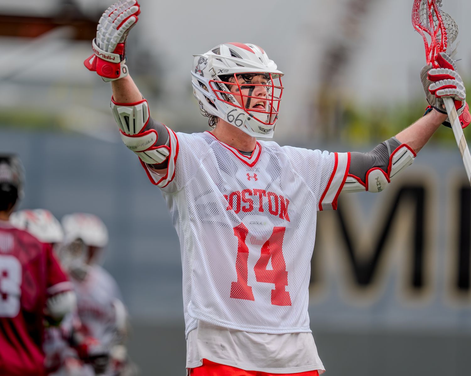Lacrosse player in white jersey celebrates during competitive match on artificial turf.