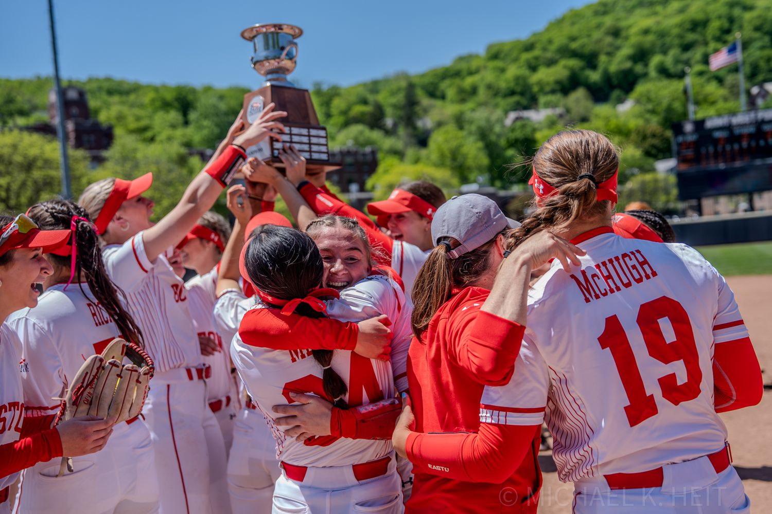 Team celebrating with trophy after victory in collegiate softball game.