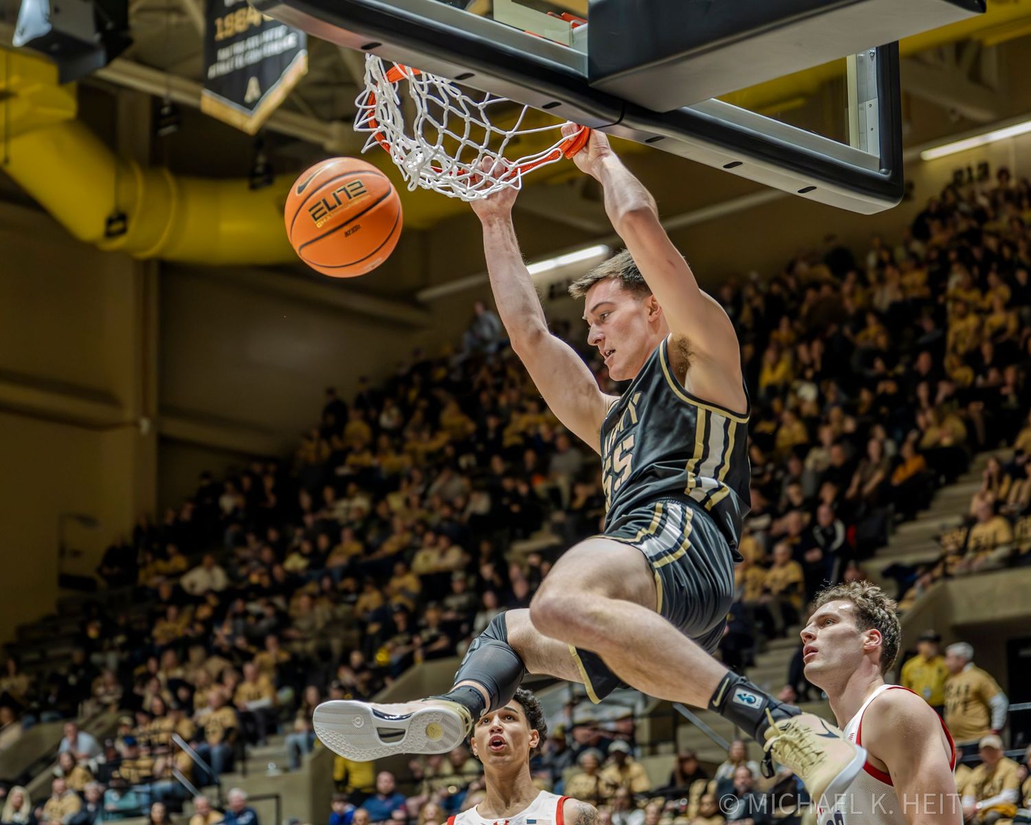A basketball player leaps high above the rim to dunk the ball during an intense game with a packed crowd watching.
