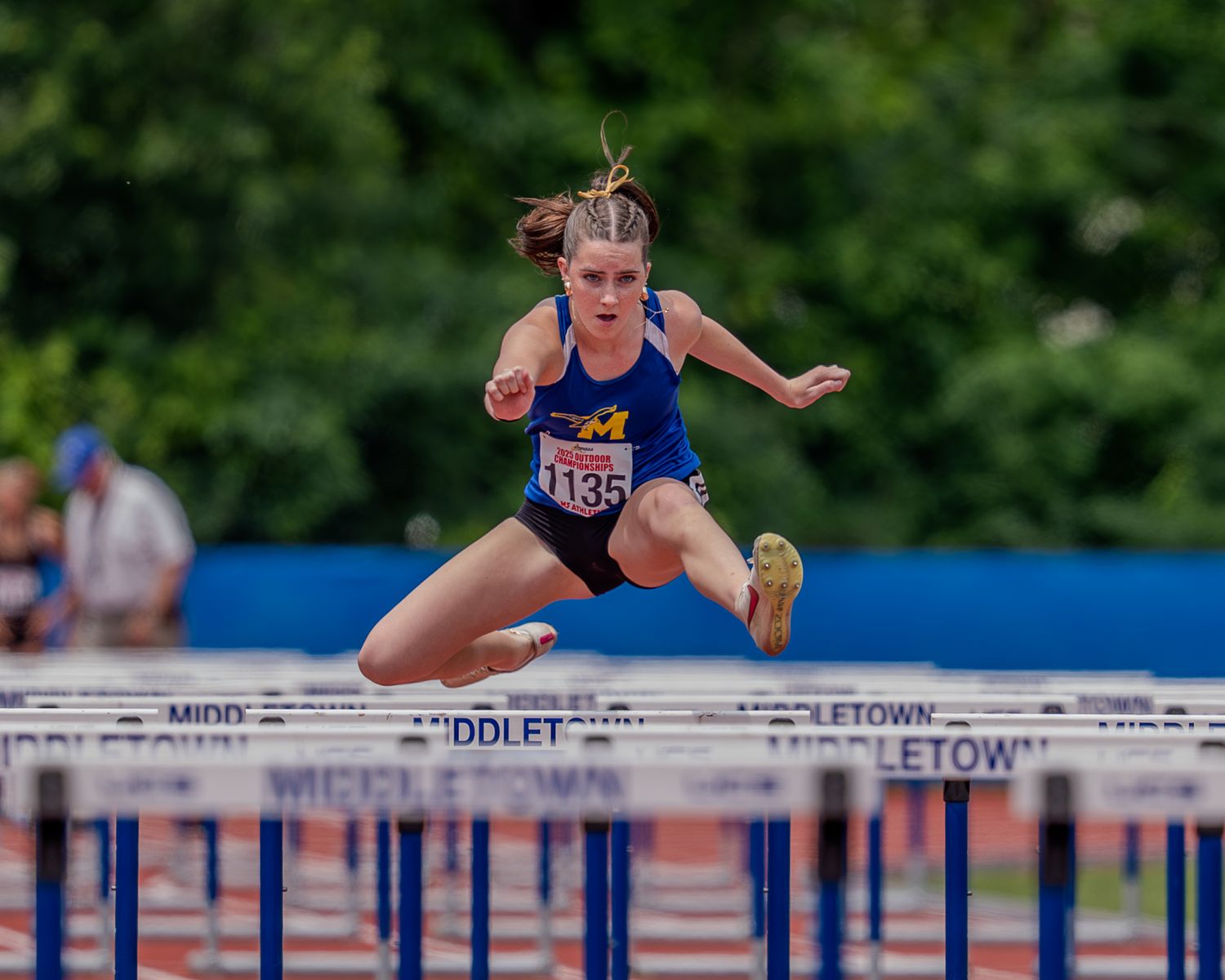 Track athlete clearing hurdles during an outdoor competition in blue uniform.