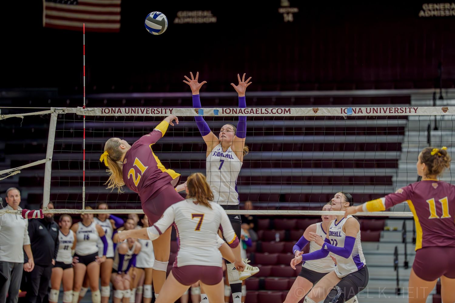 Volleyball players from two teams jump to contest the ball during an indoor match.