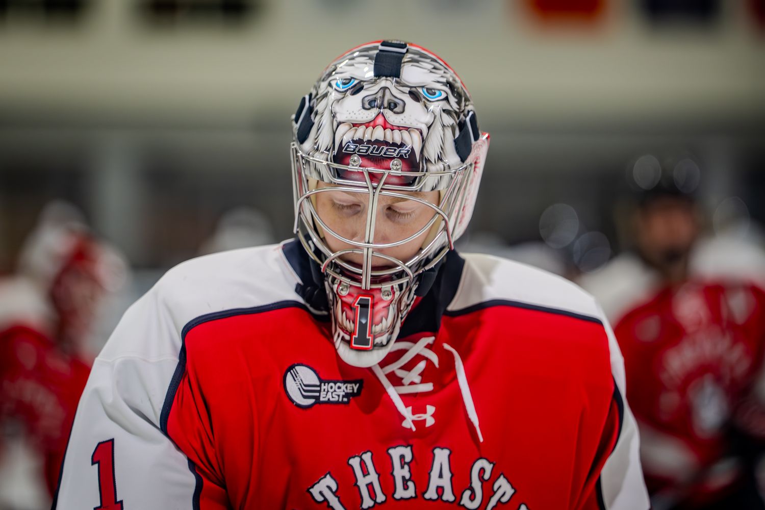A hockey goalie wearing a red jersey and protective gear stands ready in position during a game.