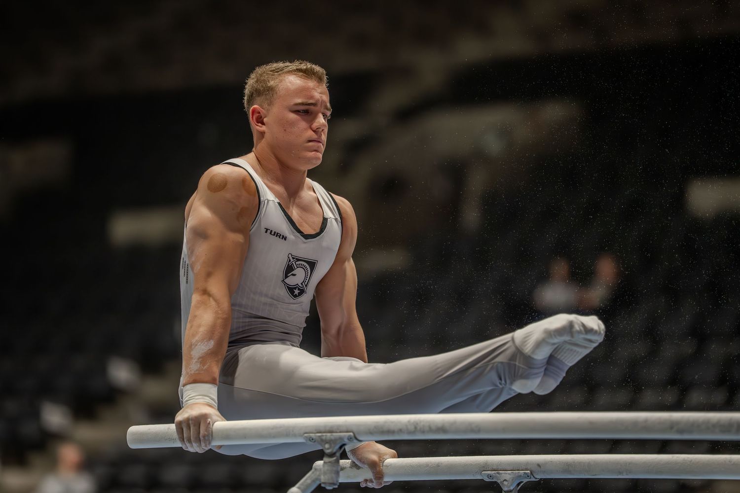 Male gymnast performing on parallel bars in a sleeveless uniform during a gymnastics competition.