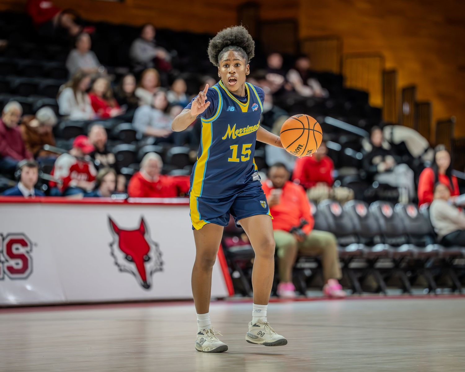 Basketball player in navy blue jersey number 15 dribbles while calling out a play during competitive game.