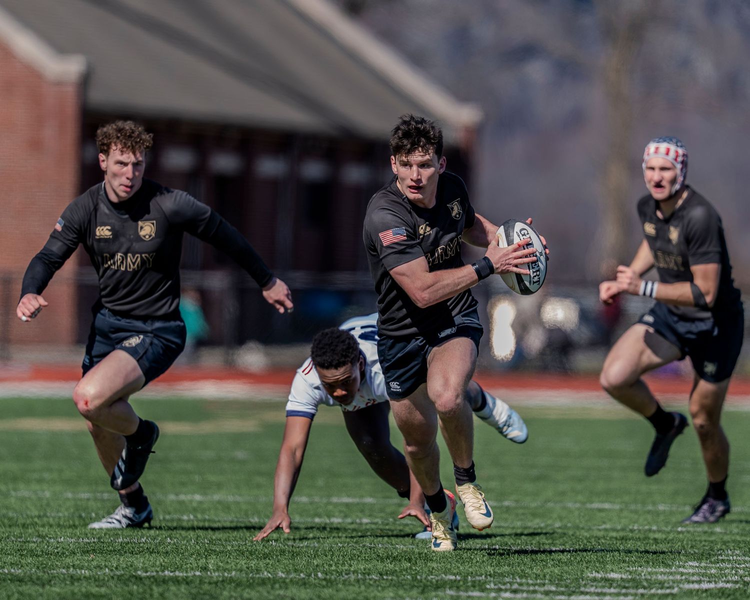 Rugby players in black uniforms crouch in a line formation during a match on a grass field.