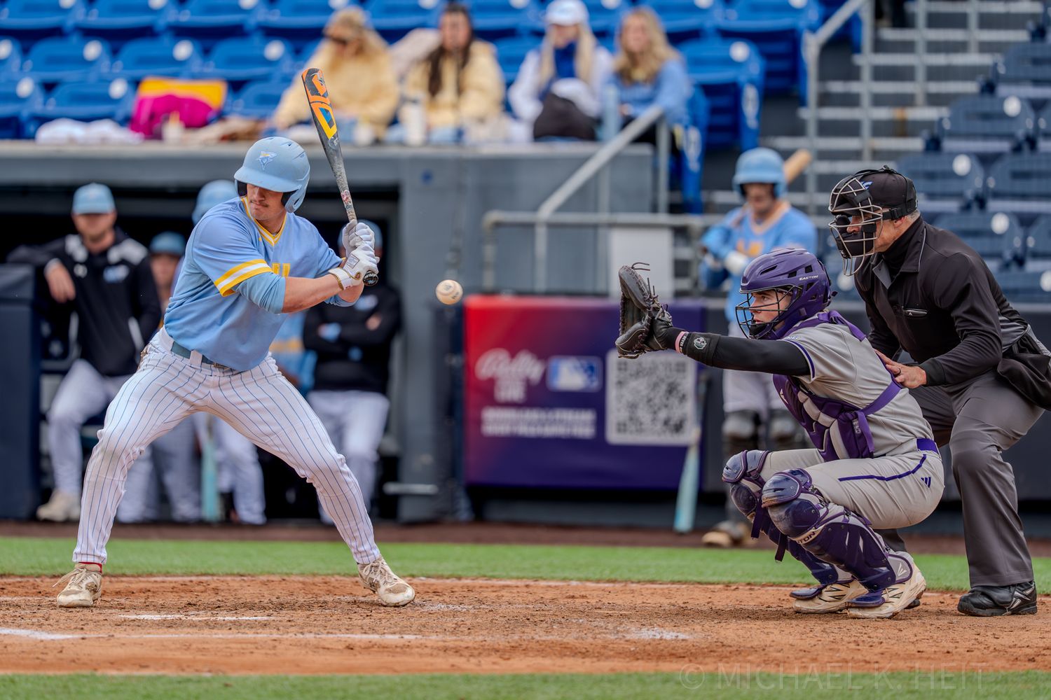 Baseball batter in light blue uniform at the plate with catcher and umpire during game action.