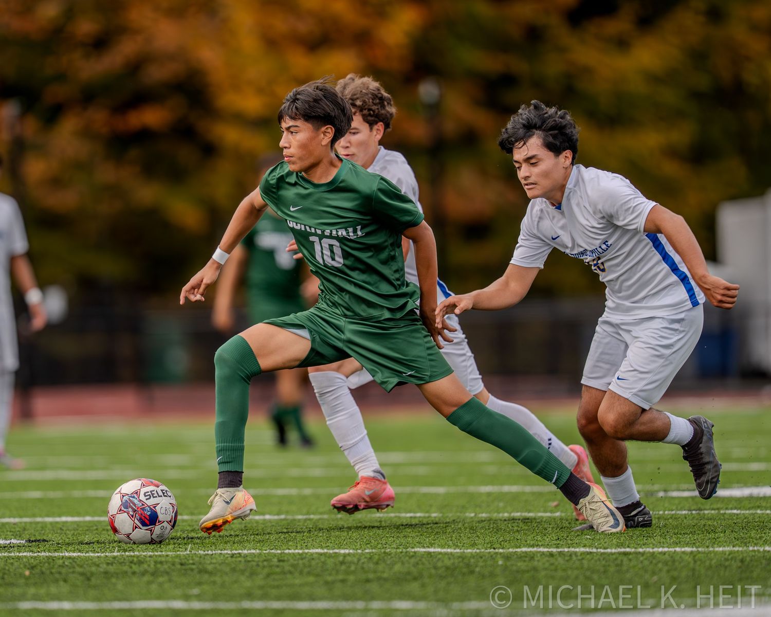 Soccer players in green and white uniforms compete for possession of the ball during an intense match.