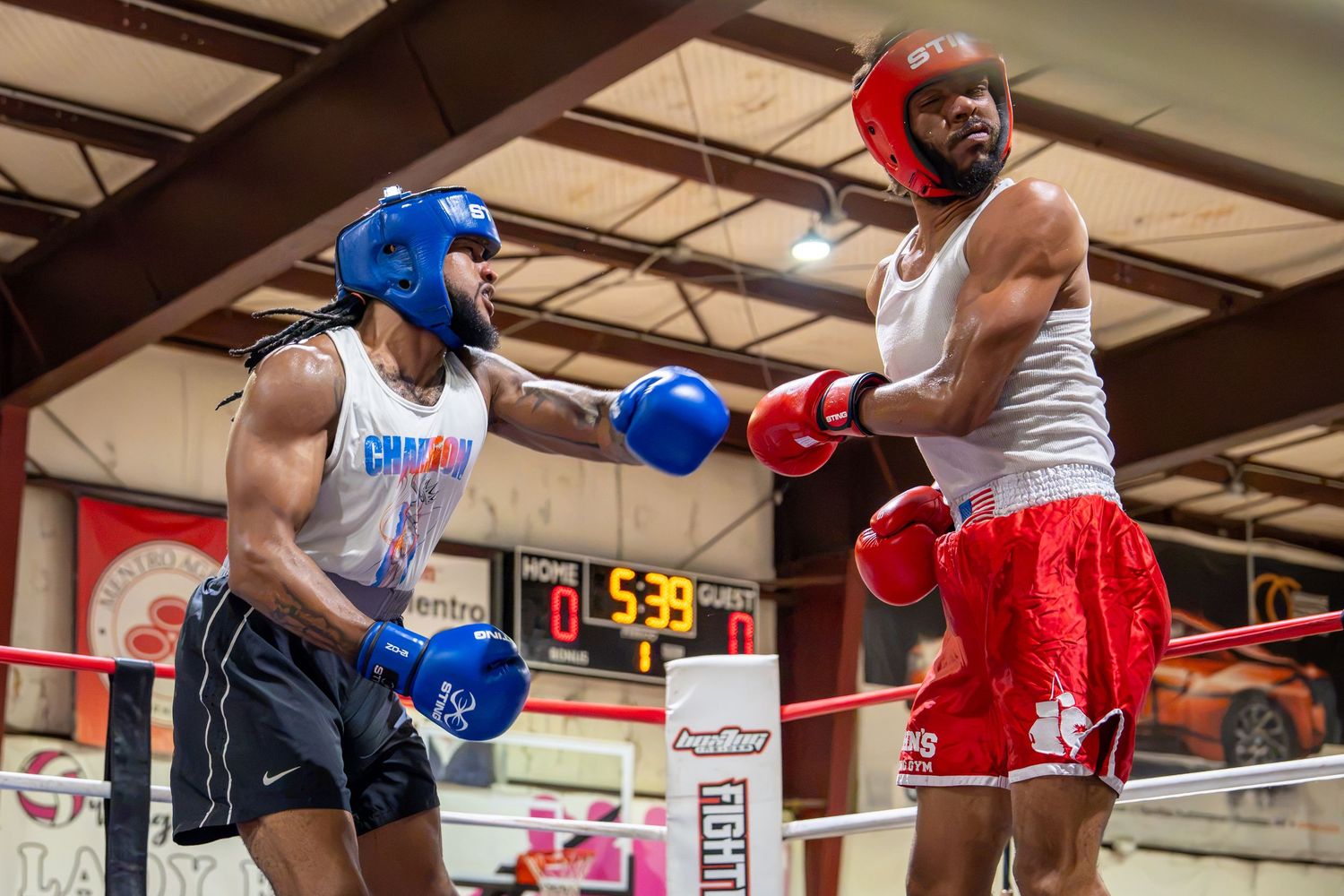 Two boxers sparring in a boxing ring, wearing red and blue gloves and headgear during an indoor match.