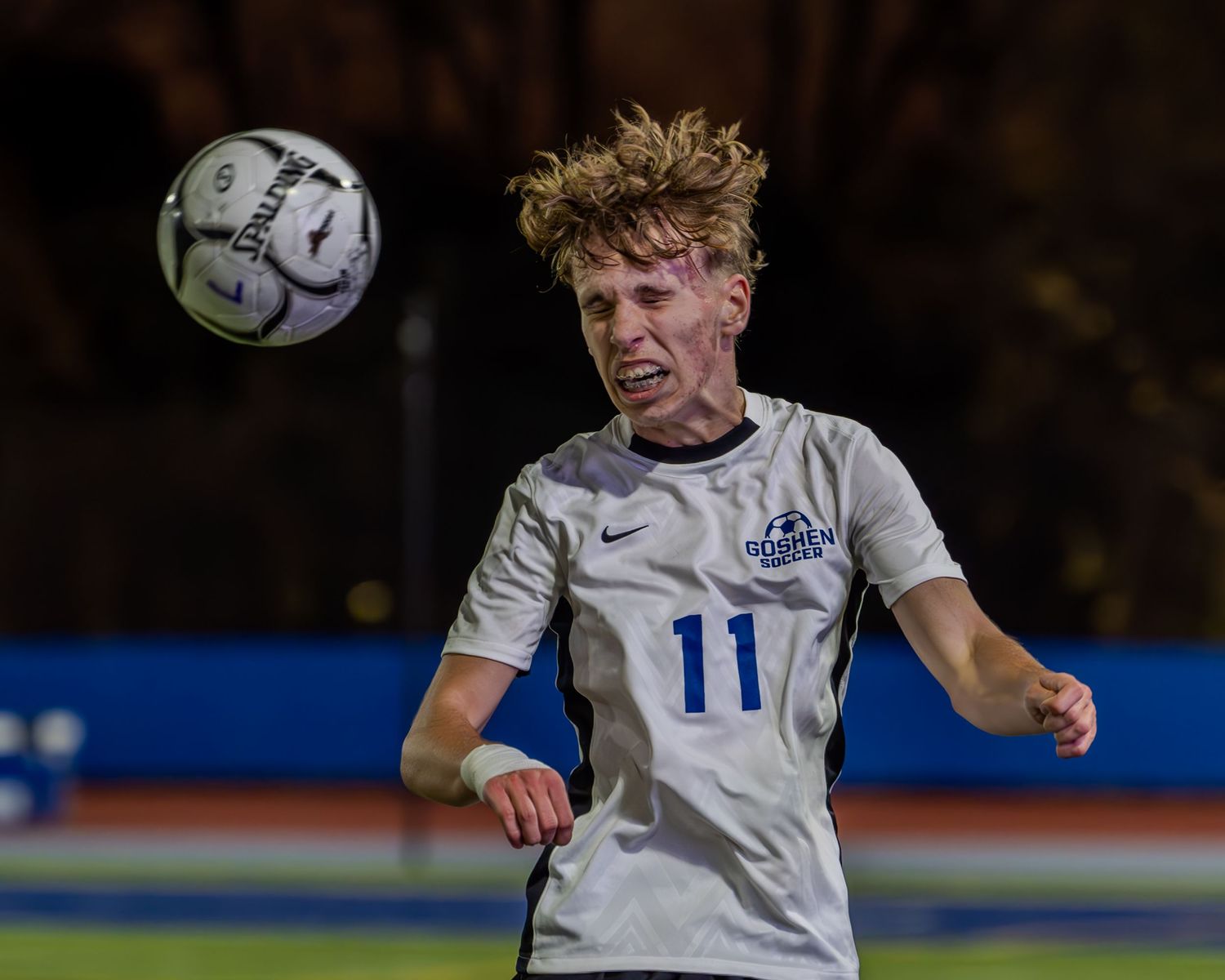 Soccer player in white jersey leaps high to head the ball during competitive match.