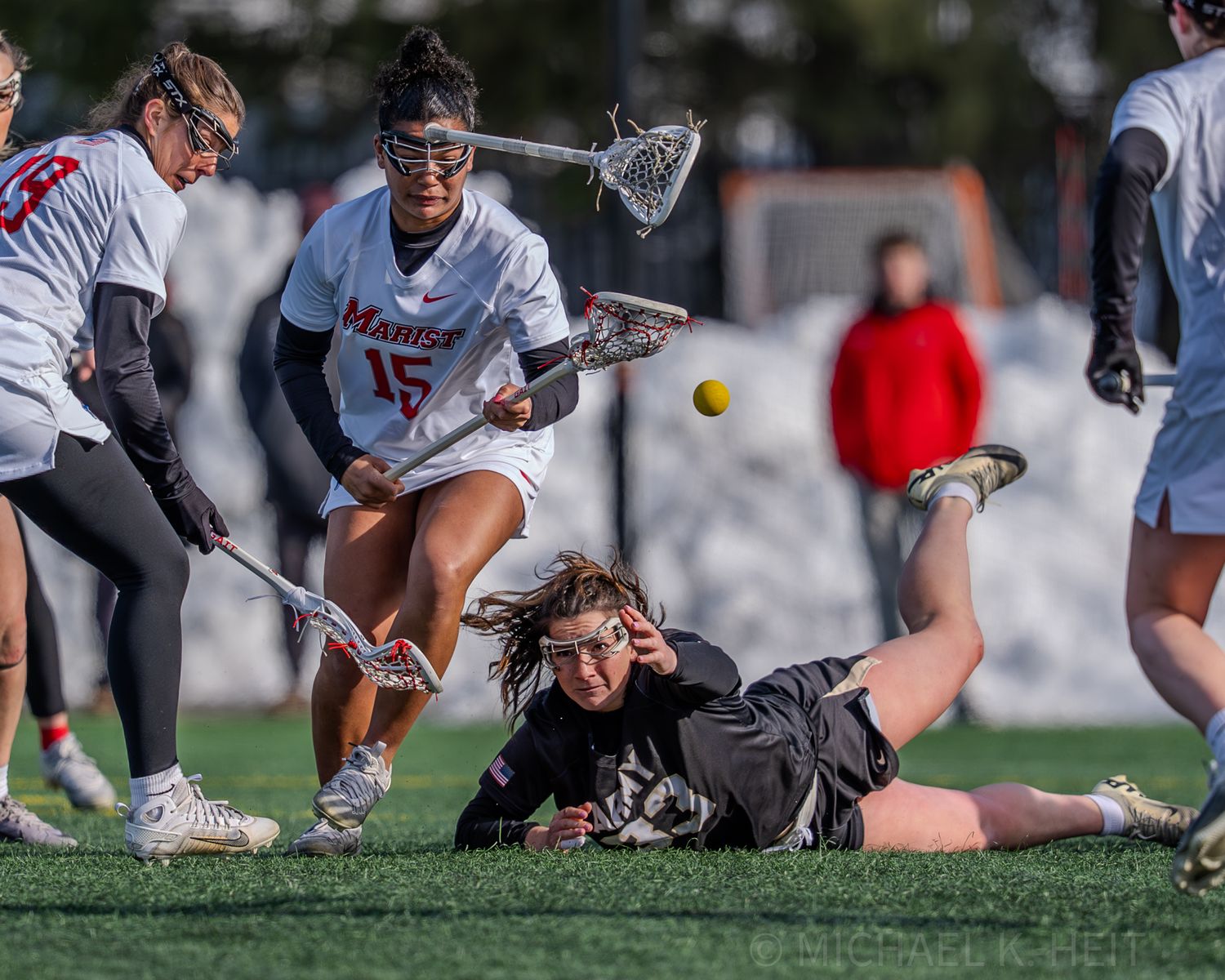 Lacrosse players dive and reach for a loose ball during competitive gameplay.