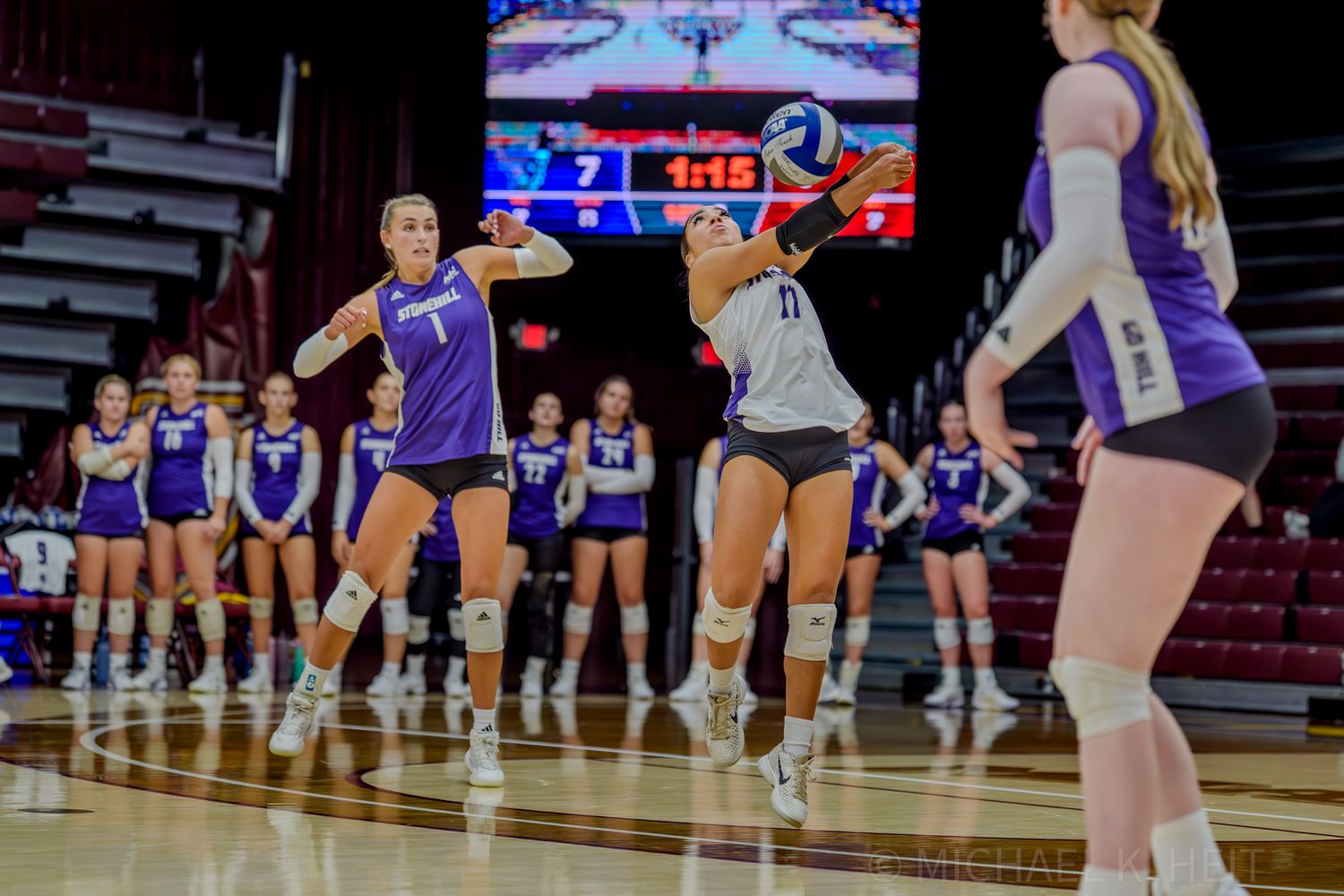 Volleyball players in defensive positions awaiting serve during match.