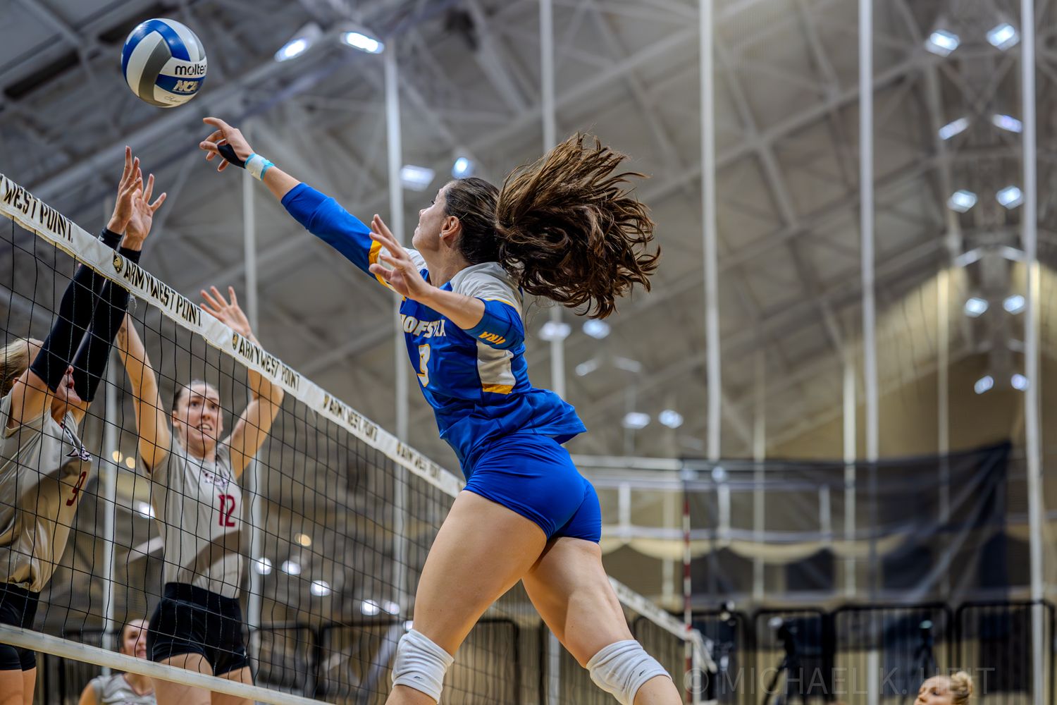 Volleyball players at the net preparing to block during an intense match.