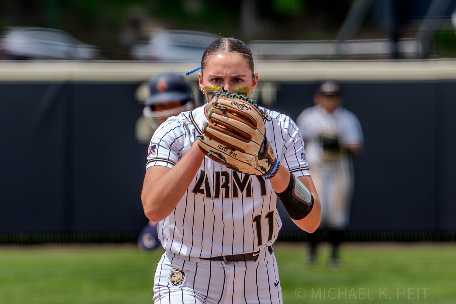 Army softball player peers over glove while preparing to pitch.