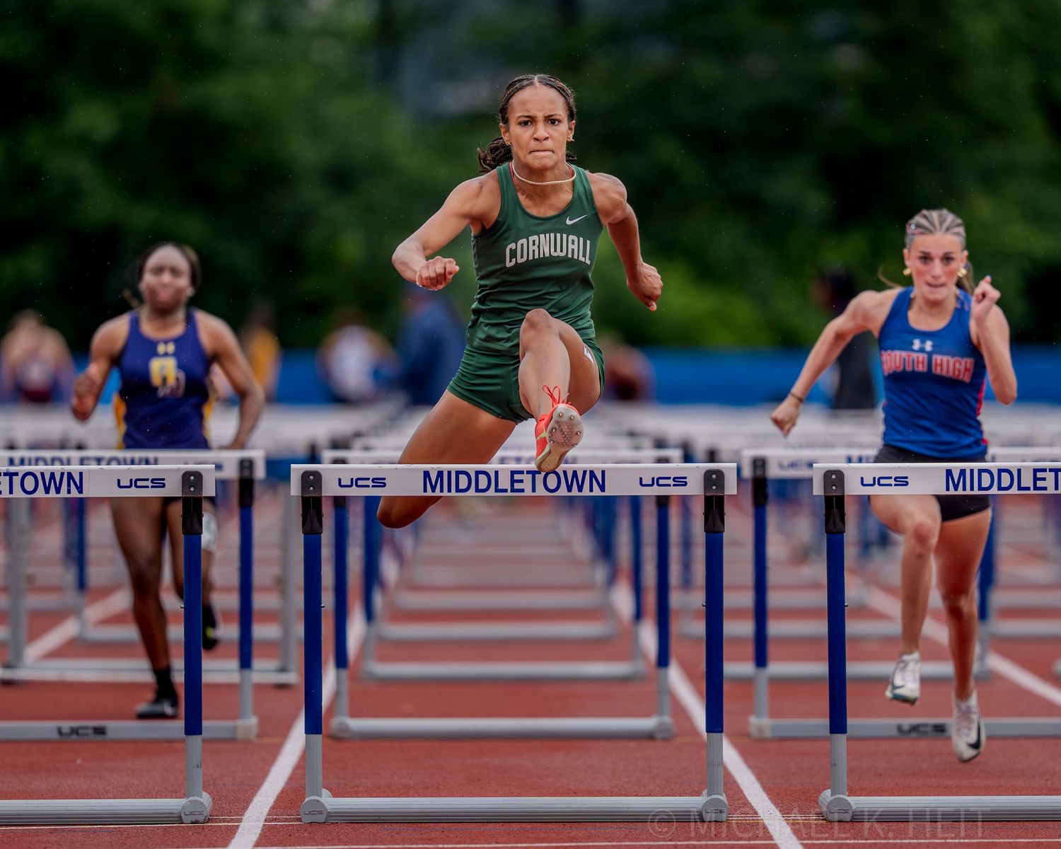 Athletes leap over hurdles during a competitive track race on a sunny day.