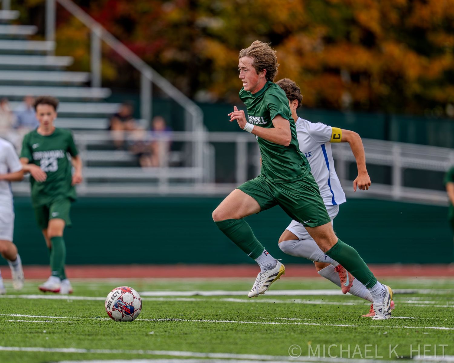 Soccer player in green jersey performs a sliding tackle during competitive match on artificial turf field.