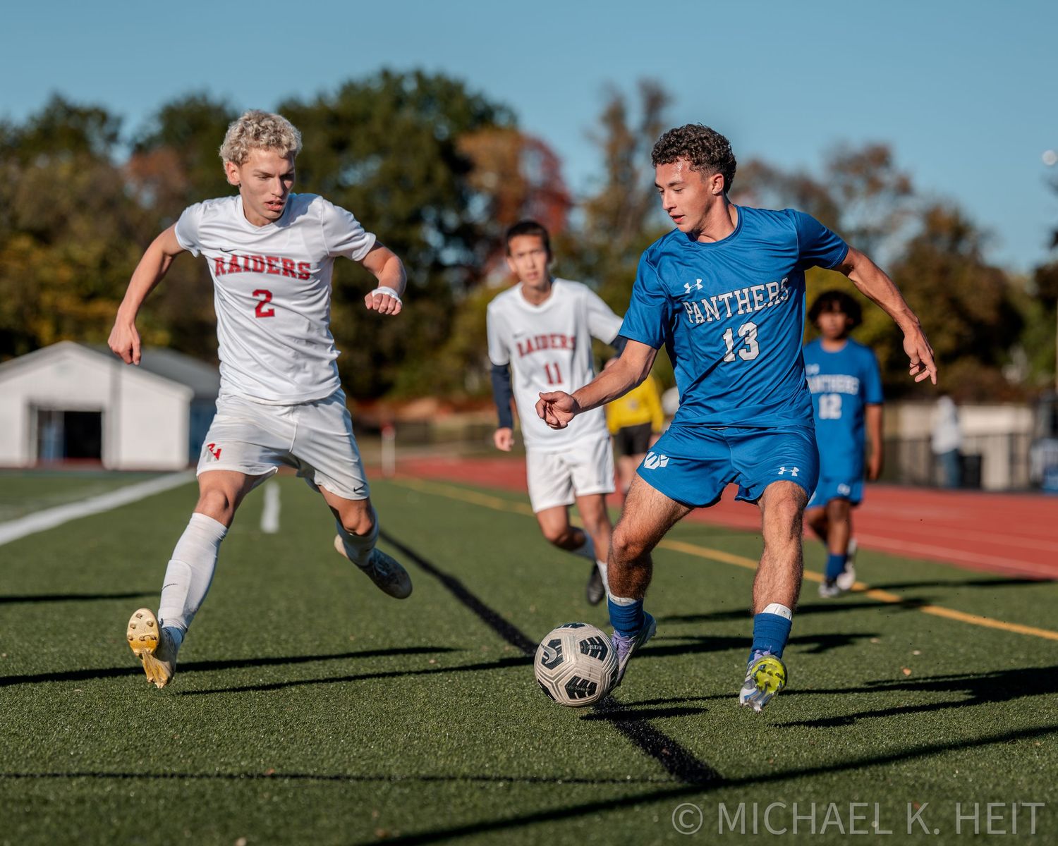 Action sequence of soccer players competing for ball control on sunny outdoor turf field.