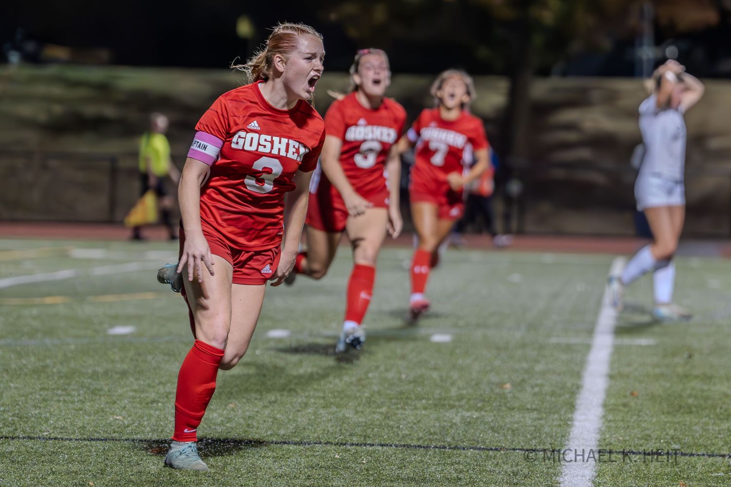 Soccer player in red uniform dribbles ball during competitive match on grass field.