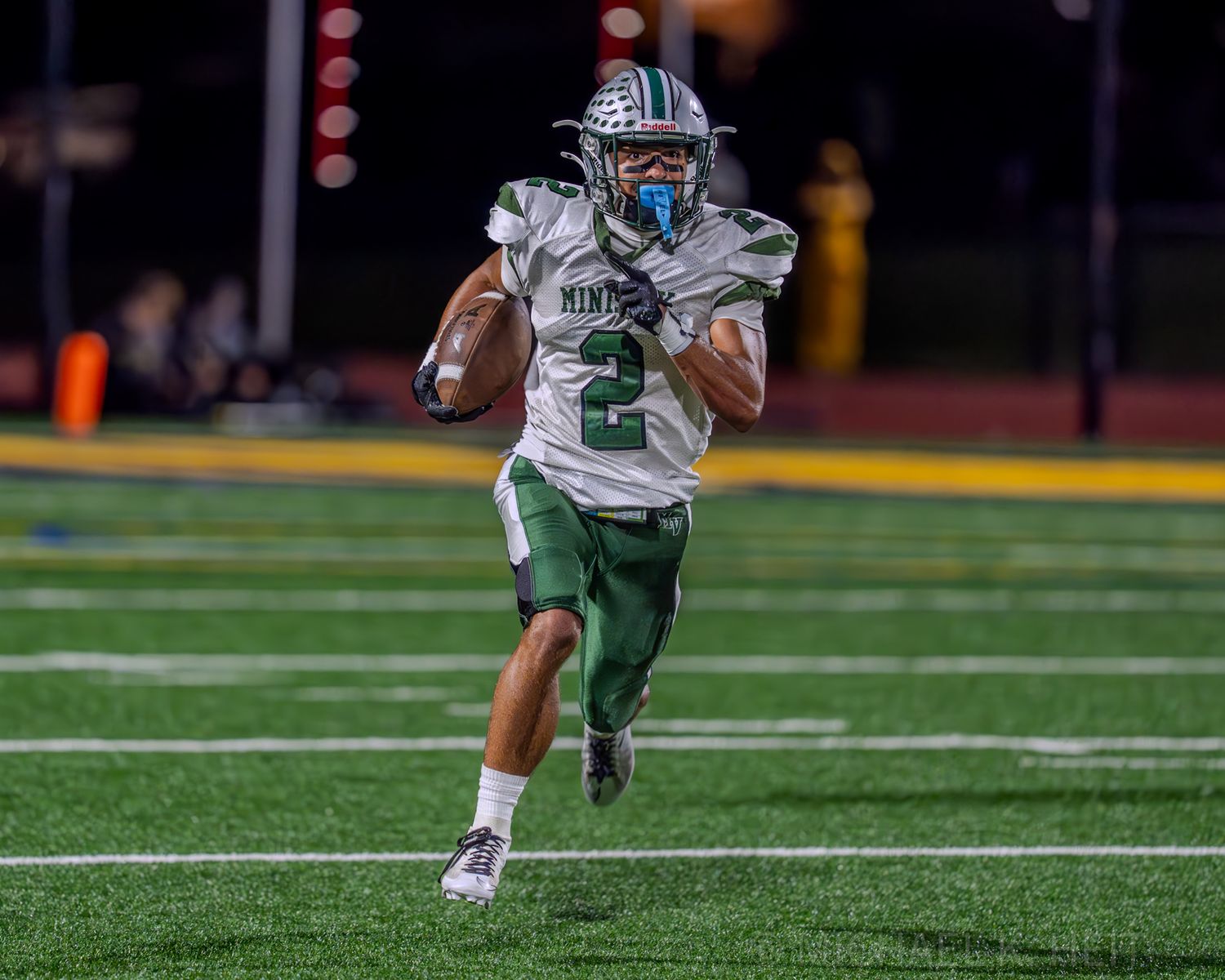 Football players in white and green uniforms compete on a well-maintained turf field.