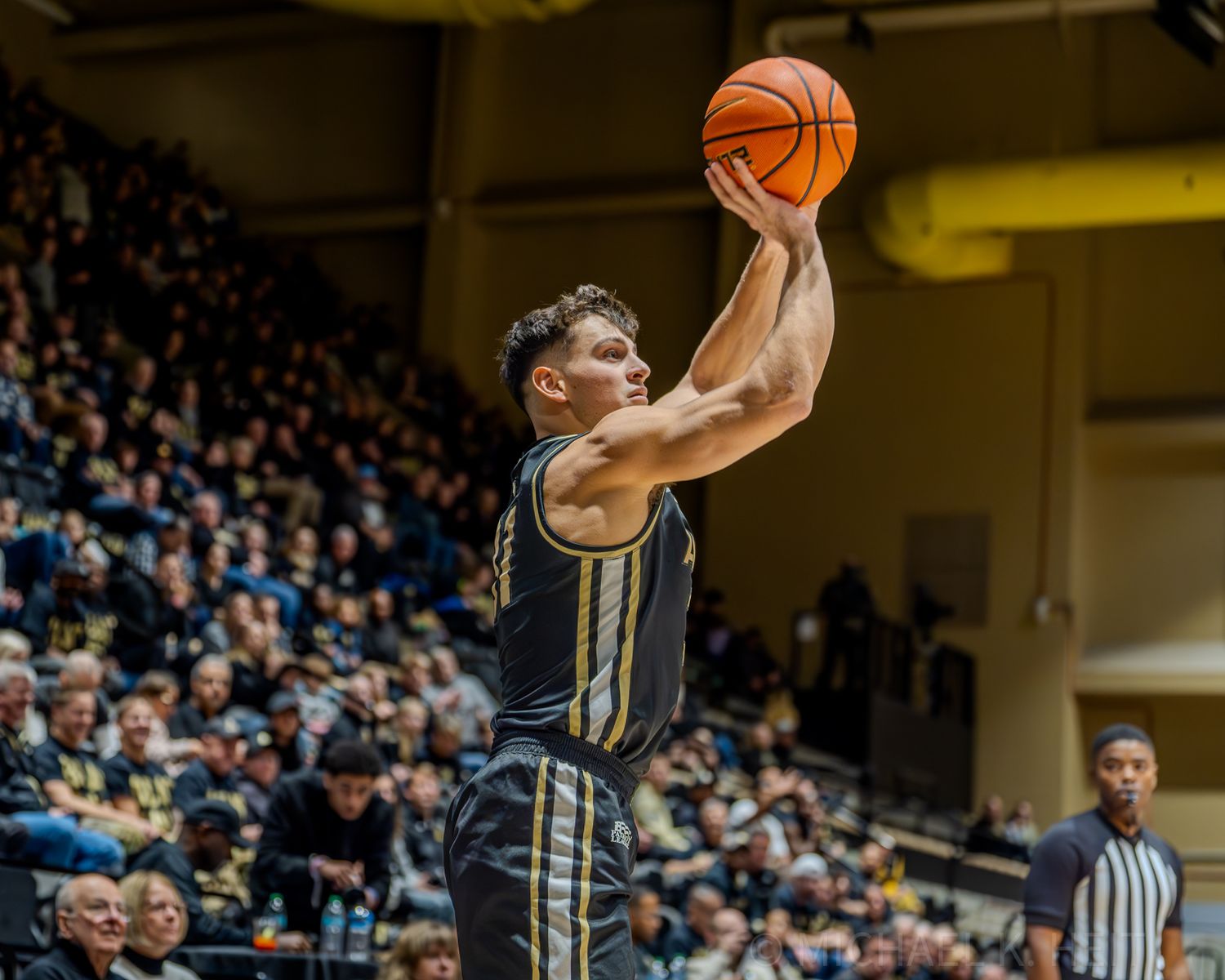 Basketball players leap high to compete for a rebound during Army-Navy game.