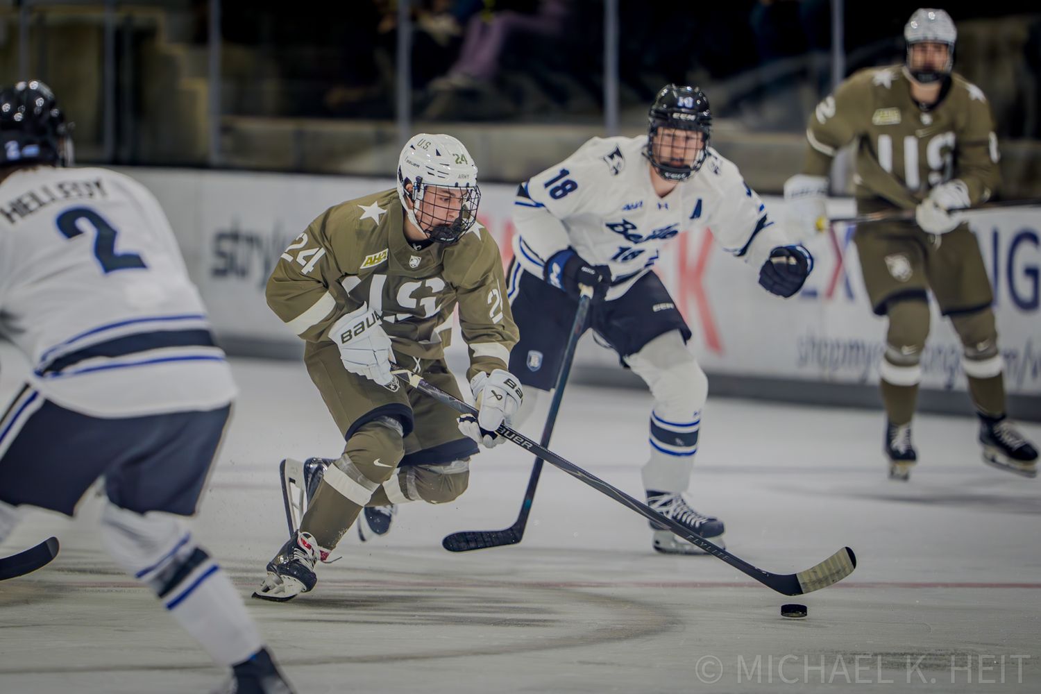 Hockey players in white and blue uniforms chase after the puck during competitive match.