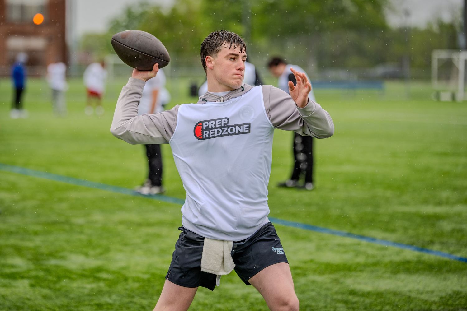 Young quarterback in Prep Redzone shirt throwing a football on a green field during practice.