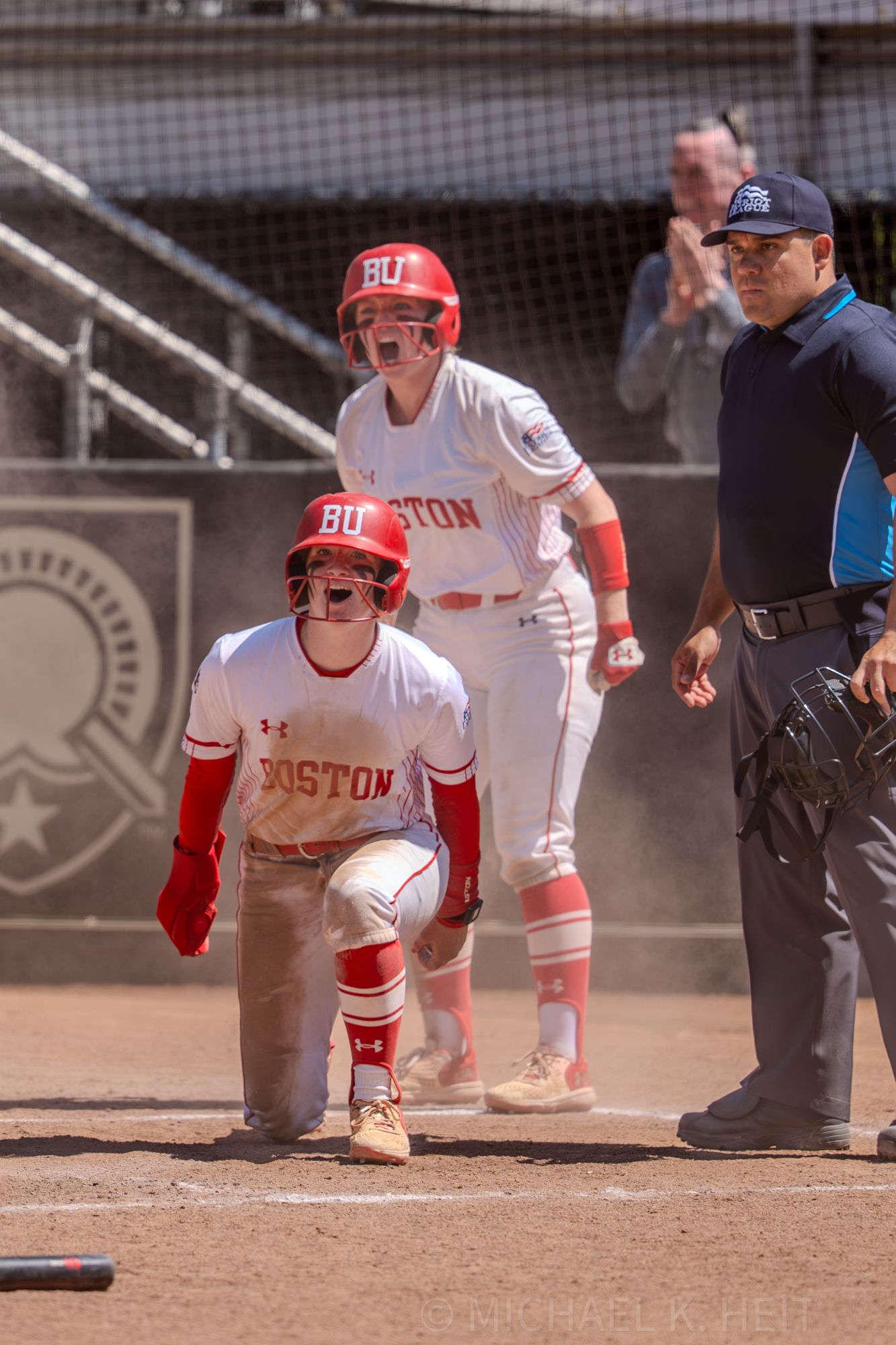 Softball players and umpire gather at home plate during Boston University game.