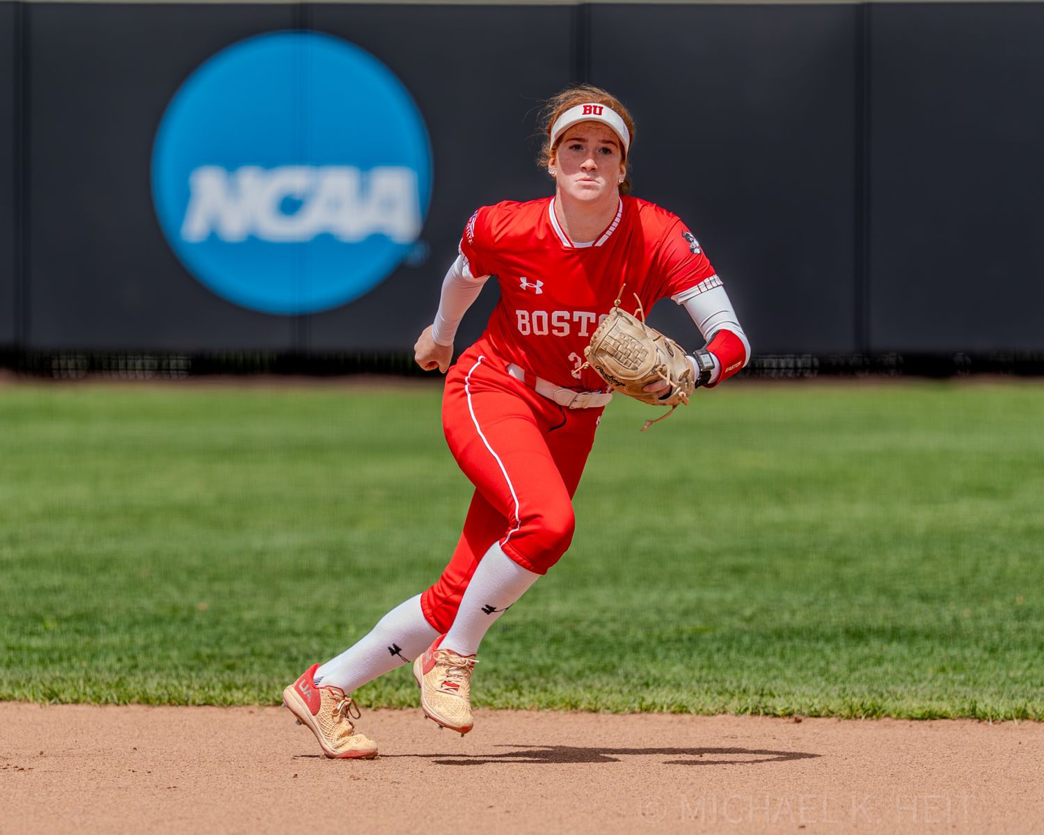 Player in red Boston uniform runs on infield with NCAA logo visible in background.