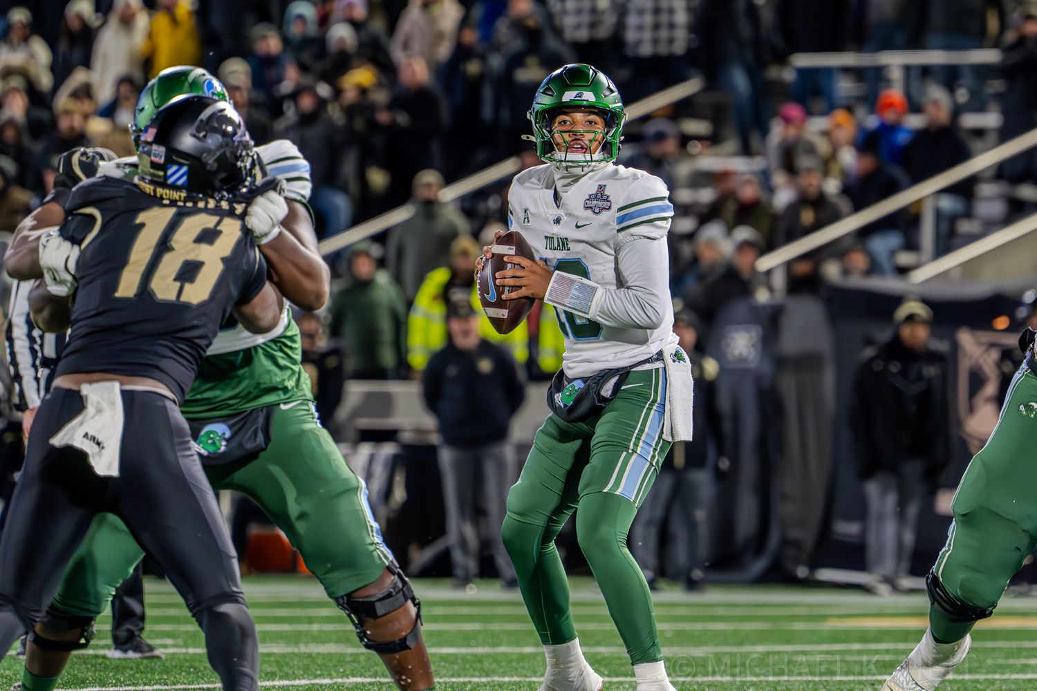 A quarterback in green uniform prepares to throw while protected by offensive line.