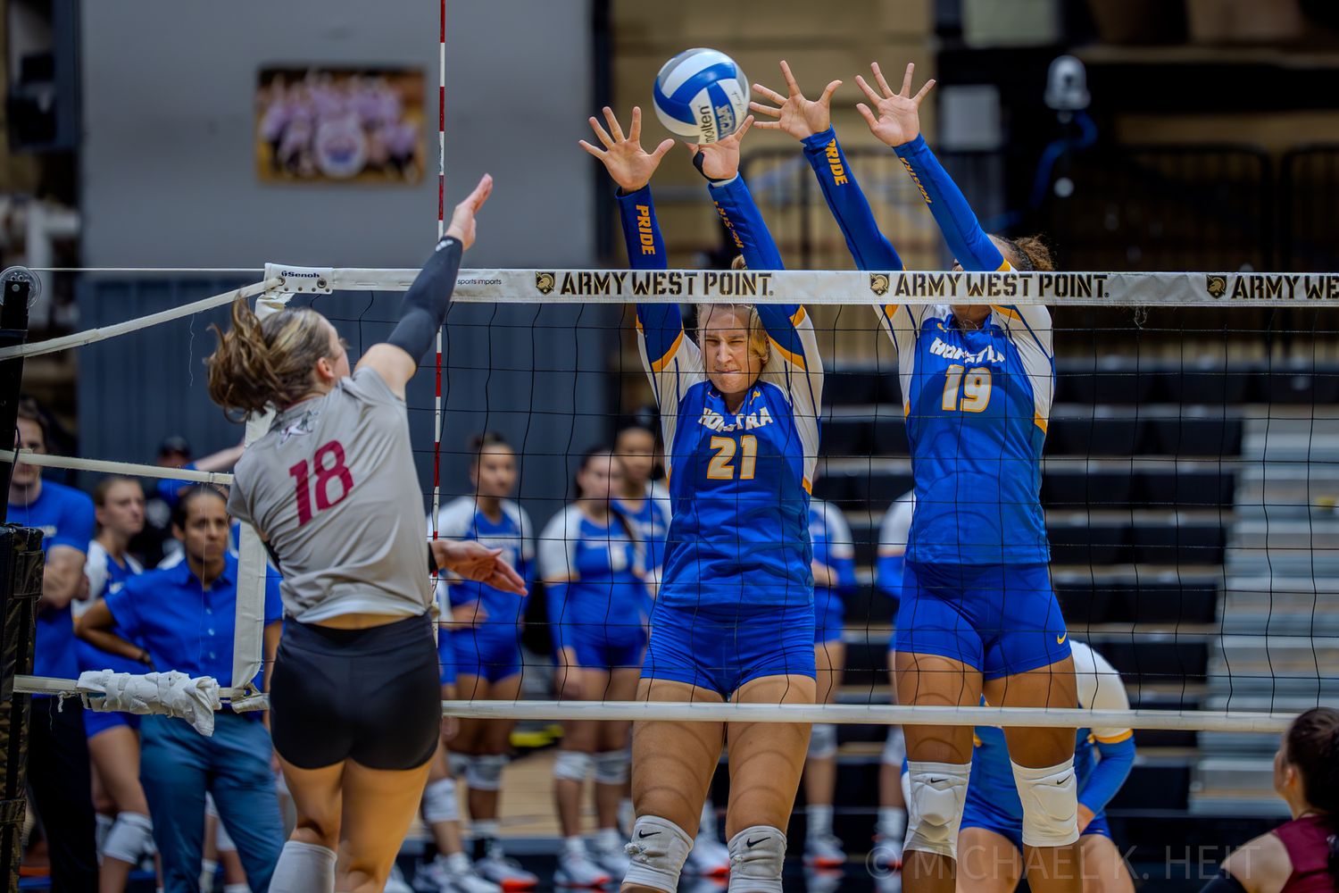 Two volleyball players jump to block a spike at the net during an intense match.
