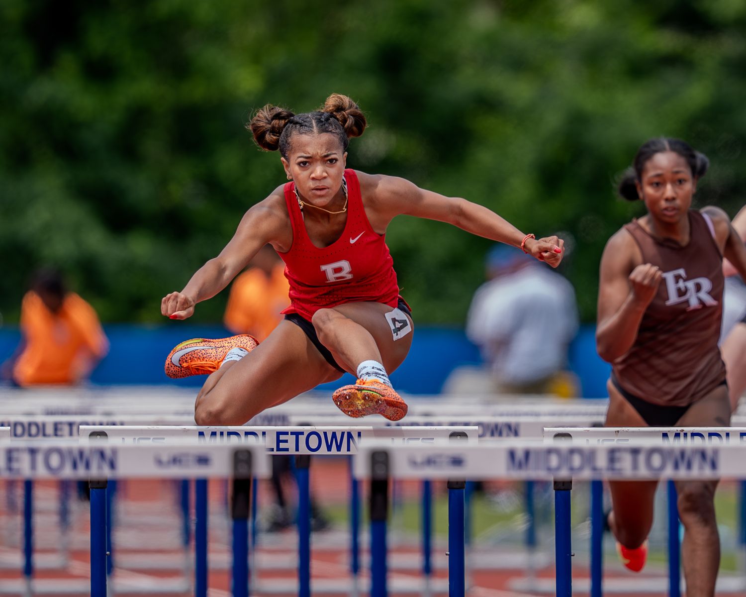 Track and field athletes competing in hurdles race during outdoor competition on blue track.