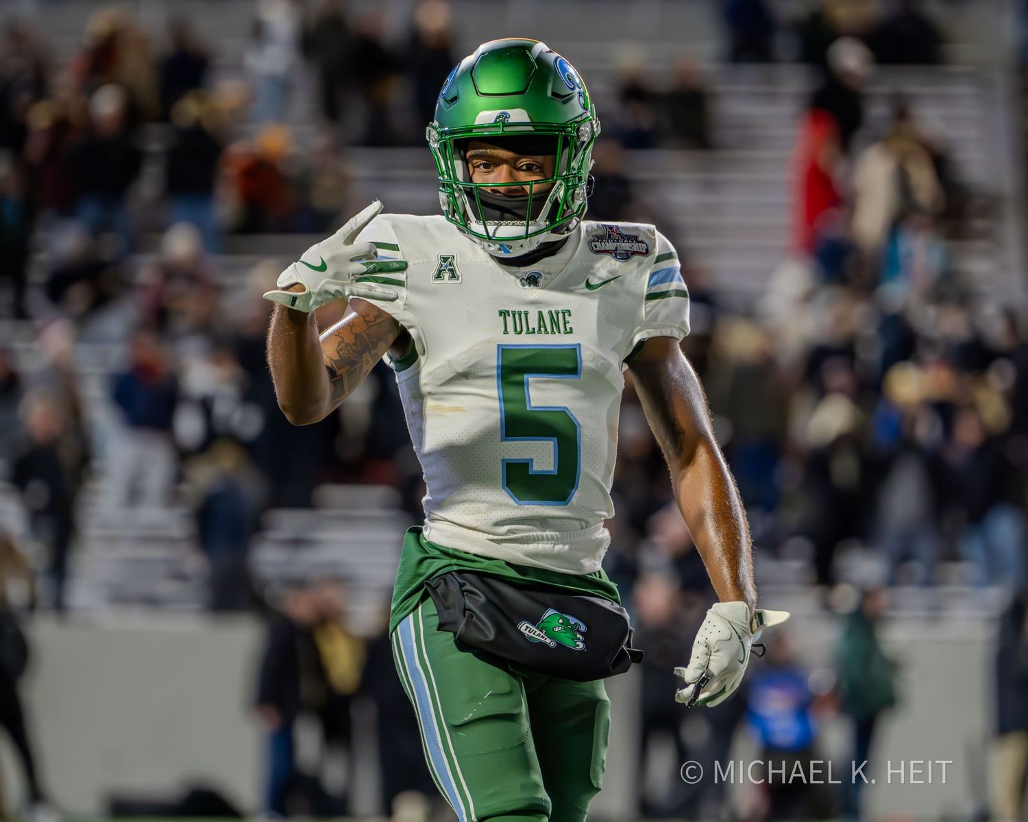 Tulane football player in green and white uniform number 5 runs with the ball during a night game.