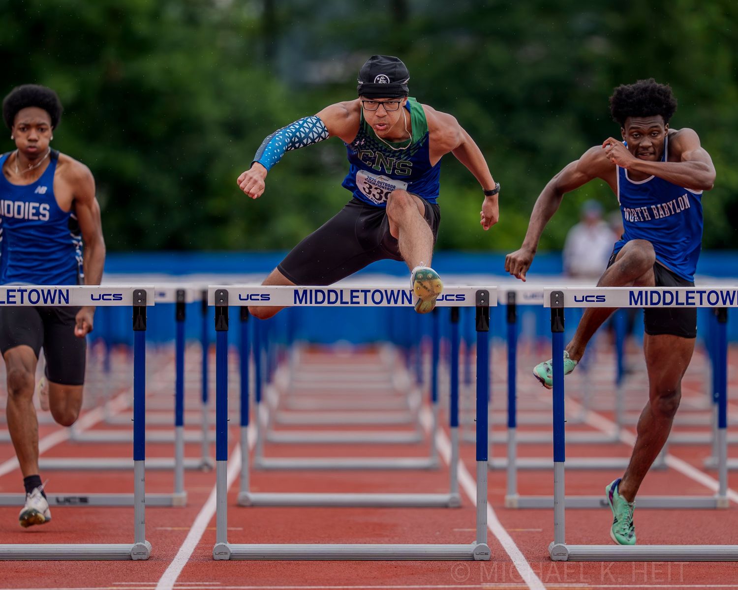 Hurdlers clear multiple barriers during an intense track competition on a blue track.