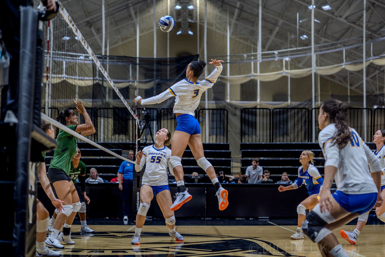 Players dive and stretch to save a volleyball during an intense indoor game.