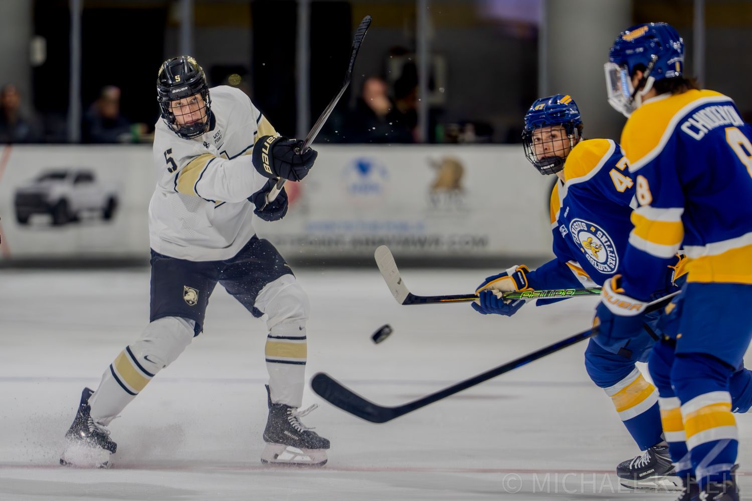 Two hockey players in white and blue jerseys battle for the puck during an intense game.