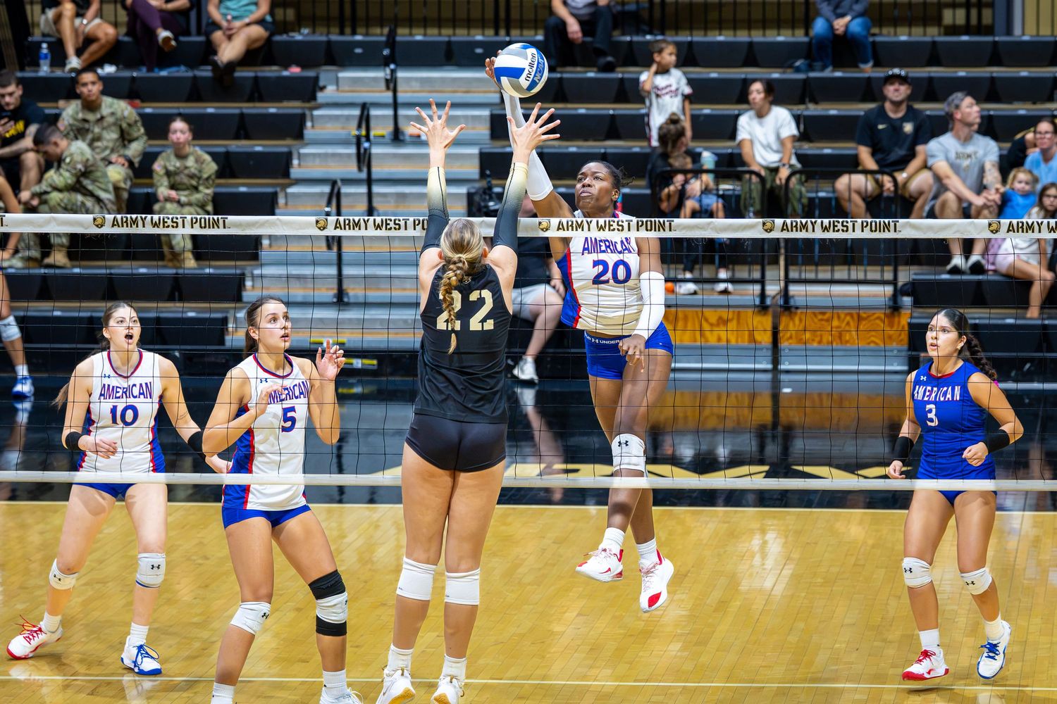 Volleyball players compete at Army West Point, with player 22 blocking a spike during an intense indoor match.