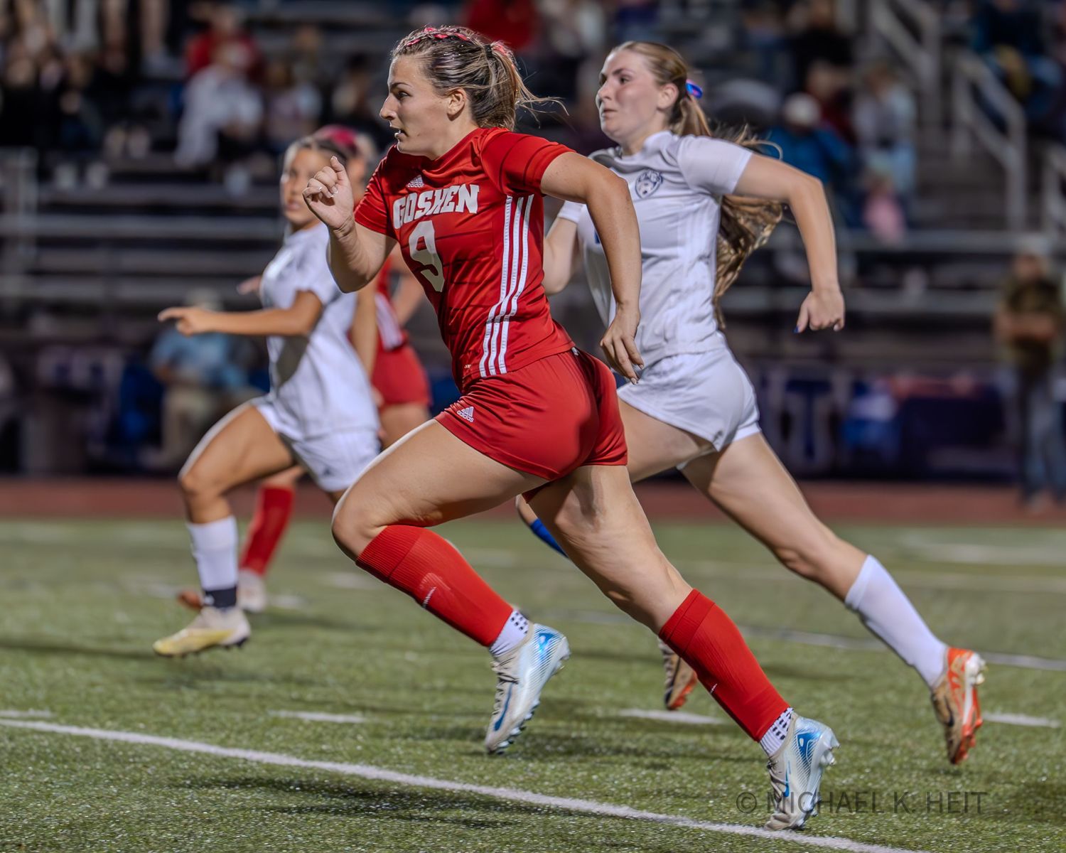 Soccer player in red uniform performs a sliding tackle against opponent in white during competitive match.