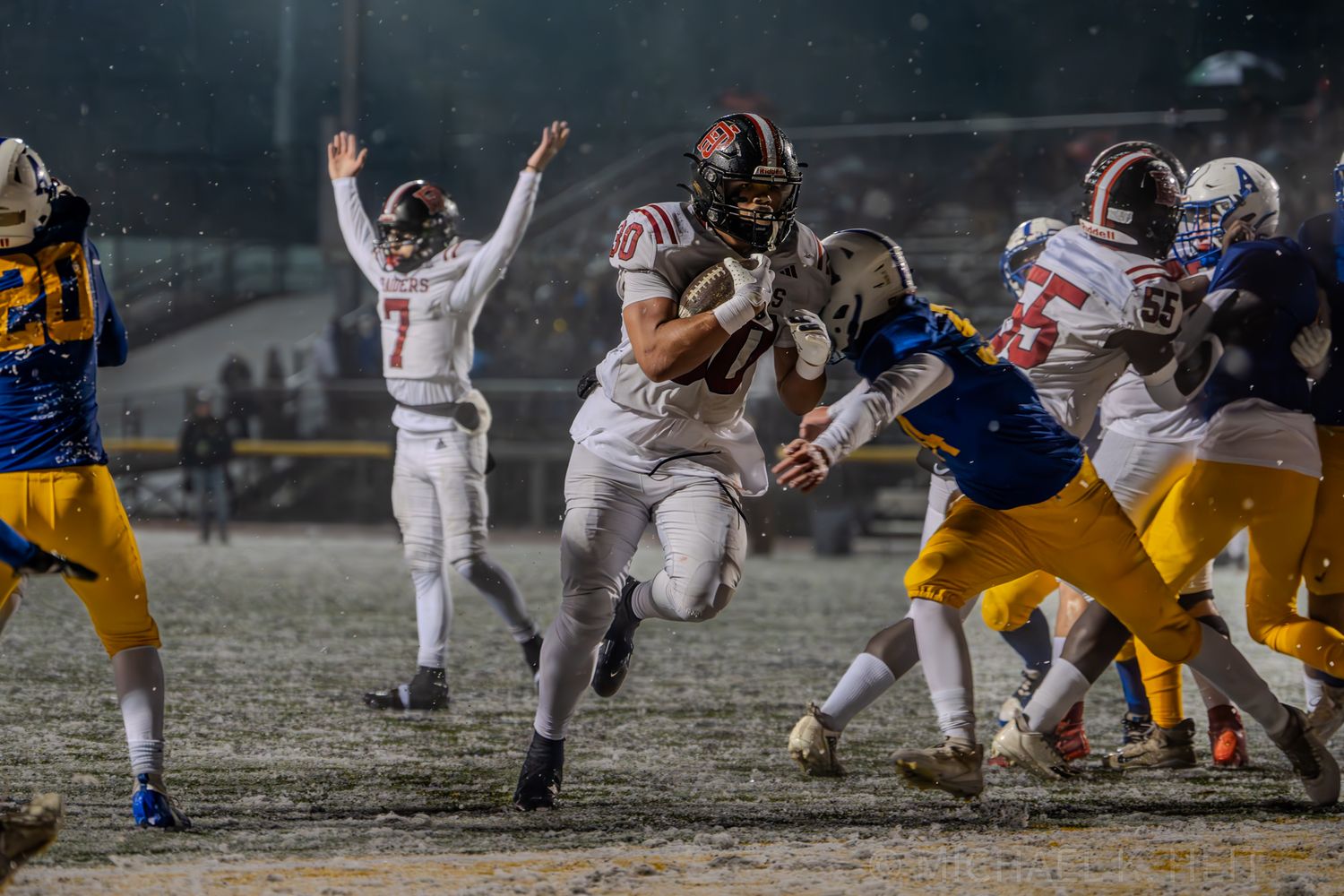 Football teams compete in snowy conditions on a dark field during a night game.