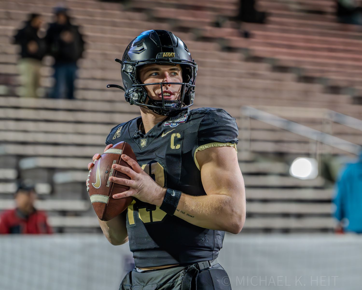 Player in black uniform holds football while scanning the field for passing options.